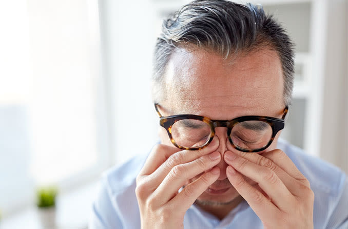 Homem grisalho de óculos esfregando os olhos para representar dor nos olhos
